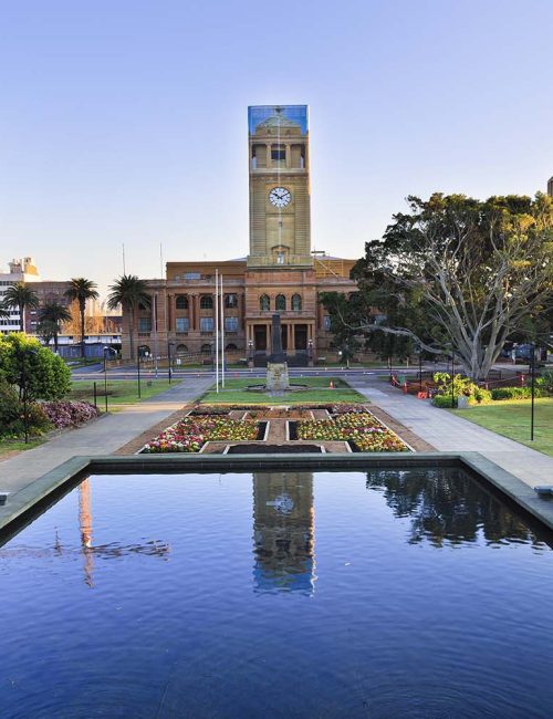 town-hall of the city of Newcastle behind still pool in a park decorated by blooming flowers at sunrise